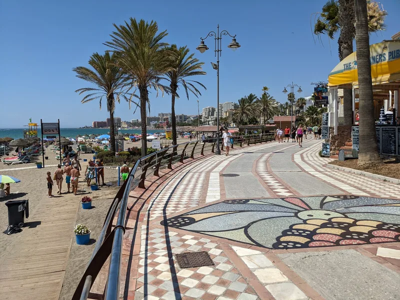 Benalmadena marina promenade at golden hour with long shadows and few visitors, white Moorish buildings catching warm evening light